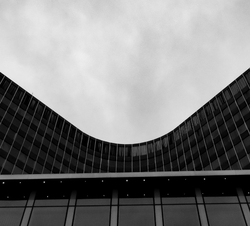 Curved concrete tower facade against an open sky, in black and white